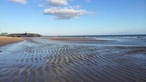 A beach with rippled sand patterns and a distant structure on the left. - Prestige Sunset Carcavelos Beach - Checkinhome (Carcavelos)
