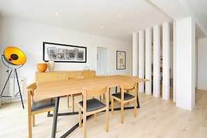 A modern dining area with a wooden table and chairs, framed artwork on the wall, and a tripod lamp.