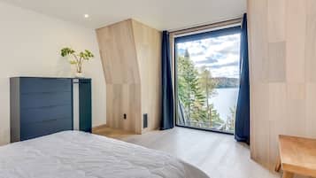 Une chambre à coucher avec un lit, une commode, une fenêtre donnant sur un lac et des arbres, et un plancher en bois.