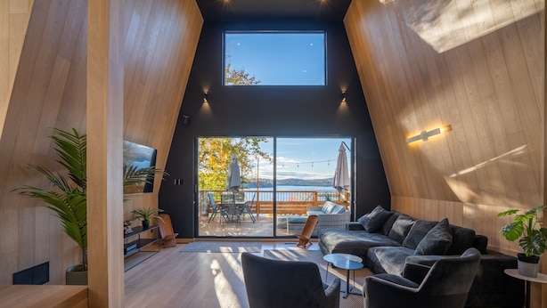 Ein modernes Interieur mit hoher Decke, Holzwänden, einem schwarzen Sofa und Blick ins Freie.