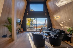 A modern interior with a high ceiling, wooden walls, a black sofa, and a view of the outdoors. - Beautiful and unique Quebec cottage: Le chêne blanc (Entrelacs)