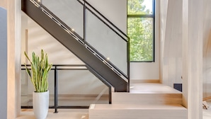 Eine moderne Treppe mit Metallgeländer, einem Blumentopf und einem großen Fenster mit Blick auf Bäume.