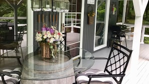 A covered outdoor area with a round glass table, black chairs, a hanging light fixture, and a welcome sign.
