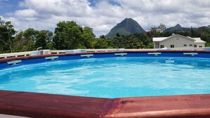 Una piscina con cubierta de madera, rodeada de abundante vegetación y una montaña al fondo.
