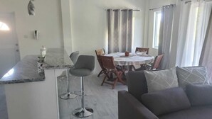 Una cocina moderna con encimera de mármol, una zona de comedor con una mesa redonda y sillas, y un sofá gris en la sala de estar.
