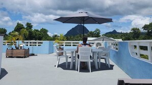 Terraza en la azotea con mesa y sillas bajo un gran paraguas, con vistas a un paisaje montañoso.