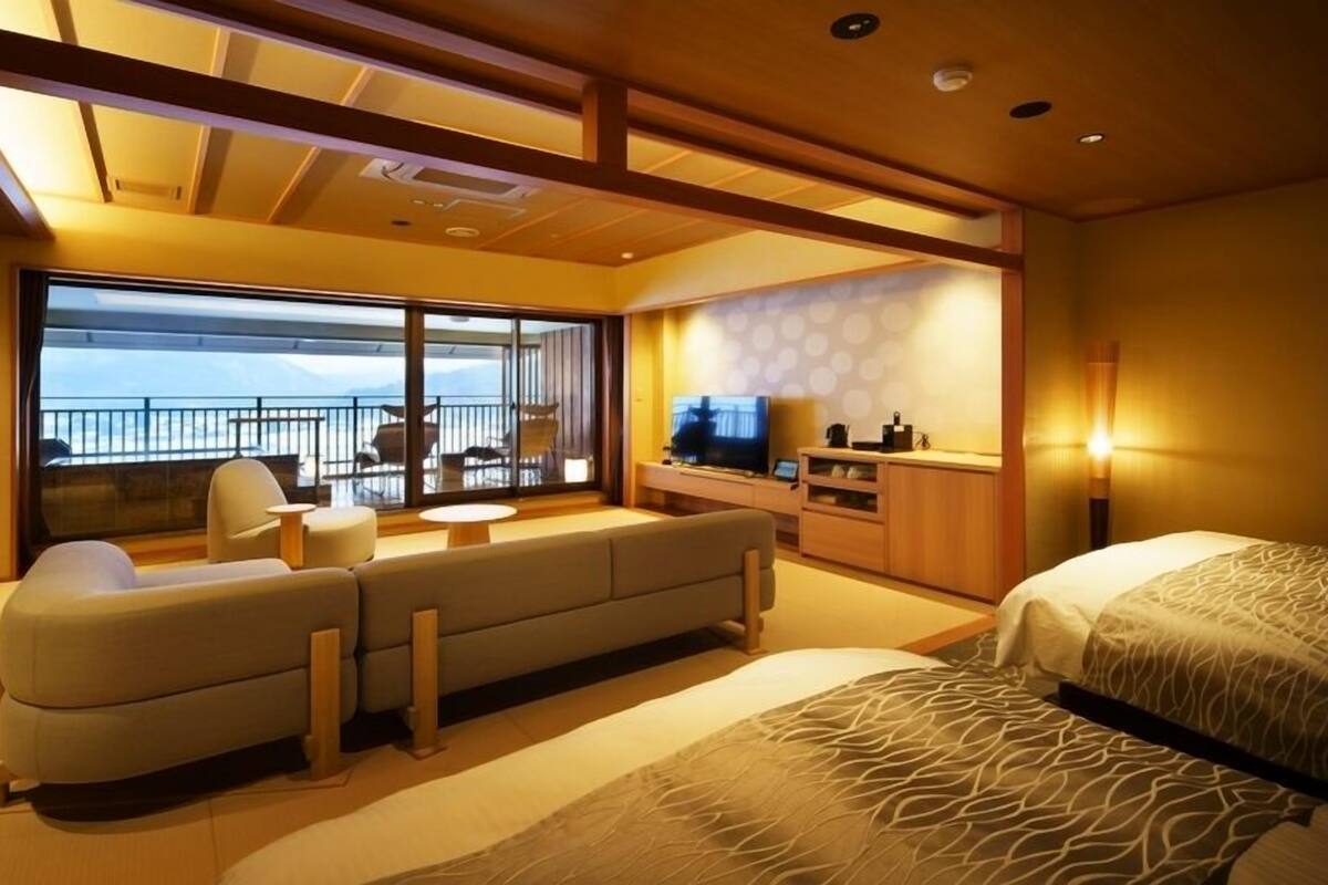 A modern hotel room with a balcony, a sofa, a bed, and a TV.