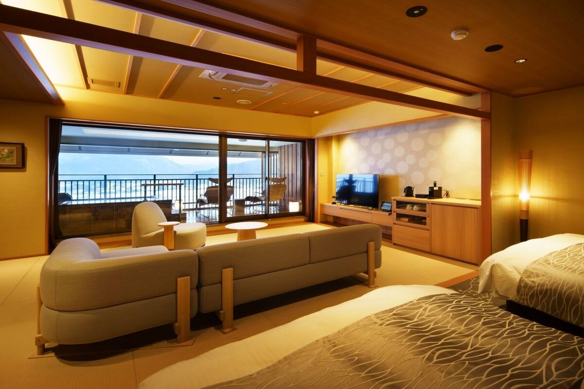 A hotel room with a sofa, a bed, a TV, and a balcony with a view.