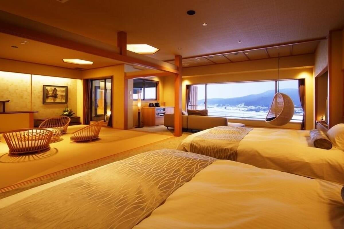 A hotel room with two beds, a hanging chair, a desk, and a view of the sea.
