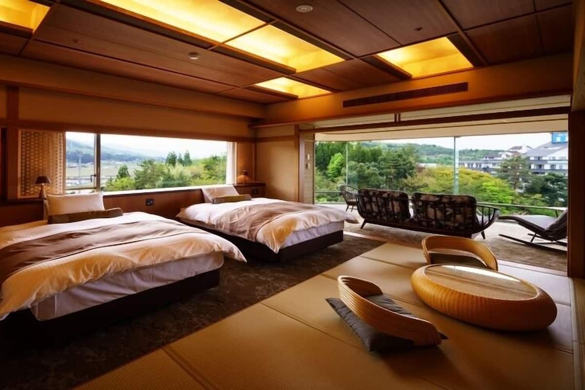 A hotel room with two beds, tatami mats, a balcony with chairs, and a view of greenery.