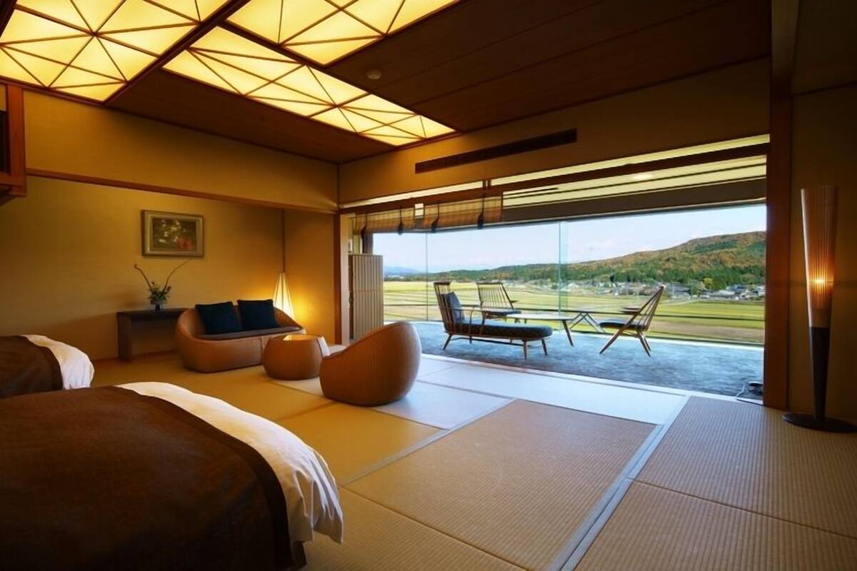 A hotel room with a large bed, a sofa, a small table, and a view of the outdoors.