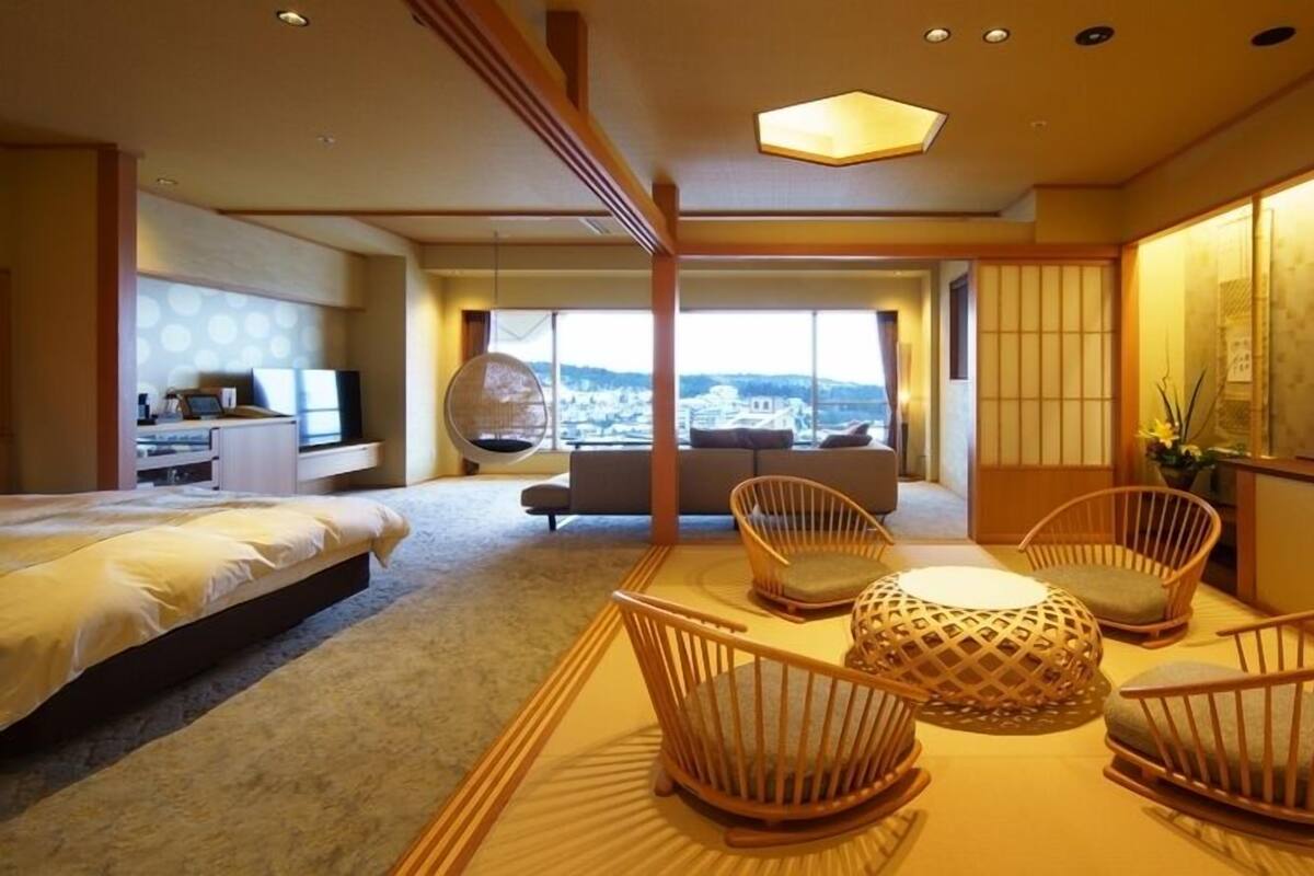 A hotel room with a bed, a seating area with chairs, a view through large windows, and a traditional Japanese sliding door.