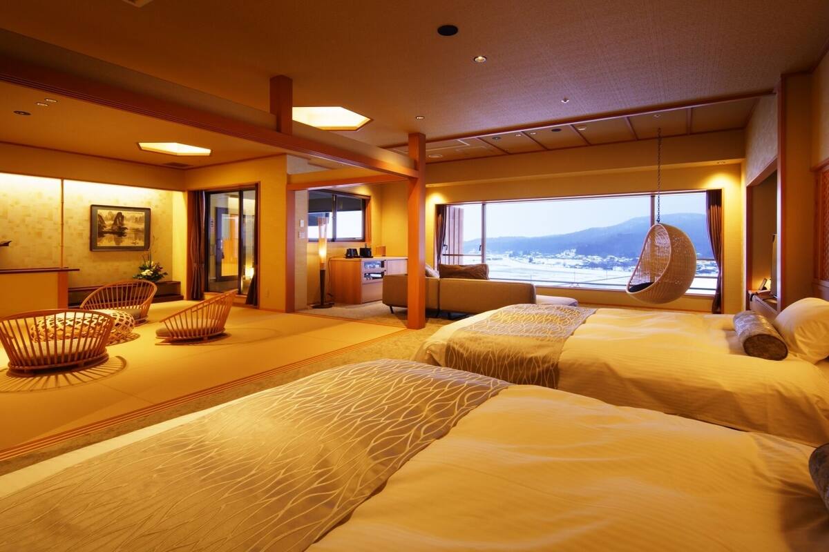 A hotel room with two beds, a sitting area with chairs, a desk, and a large window with a view.