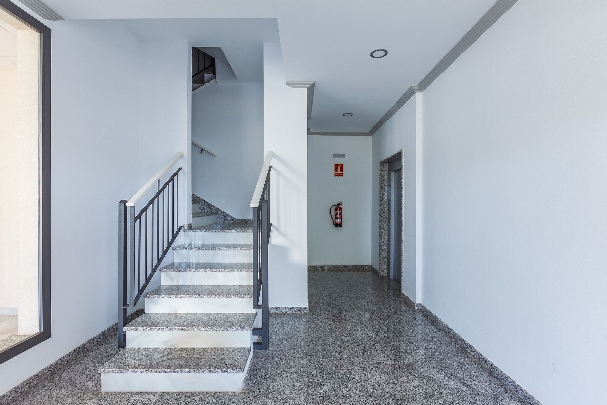 A modern interior with a staircase, a fire extinguisher, and a clean, minimalist design.
