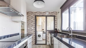 Eine moderne Küche mit integriertem Wasch- und Trockner, Edelstahlgeräten und einem großen Fenster für natürliches Licht.