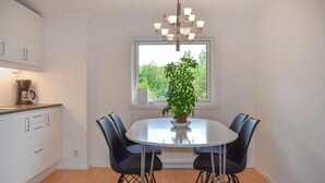 Une cuisine moderne avec une table de salle à manger ronde, des chaises noires, une machine à café et une plante en pot près d’une fenêtre.