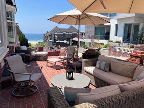 Une terrasse avec des meubles d’extérieur, un grand parasol et une vue sur l’océan.