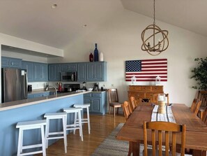 A modern kitchen with blue cabinets, a central island, and a dining area with a wooden table and chairs. - Walk to Shops! 3 Story Condo w/ Views + Elevator (Fish Creek)