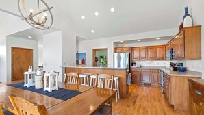 A spacious kitchen with wooden cabinets, a central island, and a dining area with a wooden table and chairs. - Walk to Shops! 3 Story Condo w/ Views + Elevator (Fish Creek)