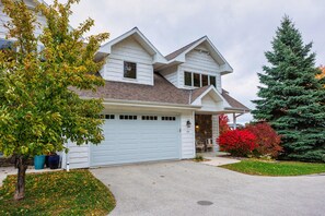 A two-story house with a garage, a driveway, and a well-maintained lawn. - Walk to Shops! 3 Story Condo w/ Views + Elevator (Fish Creek)