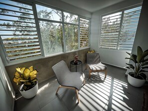 A sunlit room with large windows, two chairs, a small table, and potted plants. - 3 BR. Residence w. Rooftop Access (San Juan)