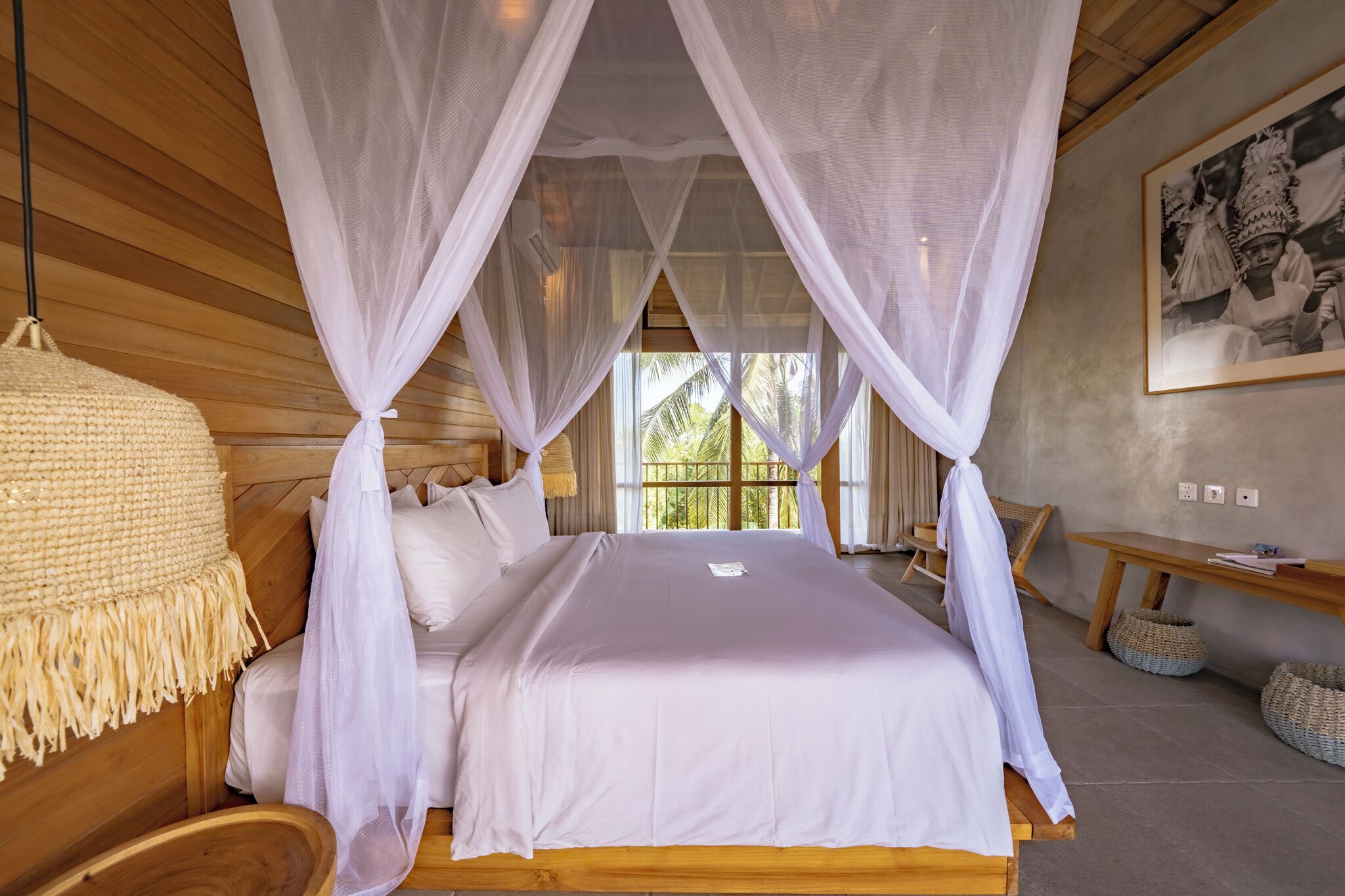 A room with a bed under a canopy, a woven rug, a bench, and a wall-mounted picture.