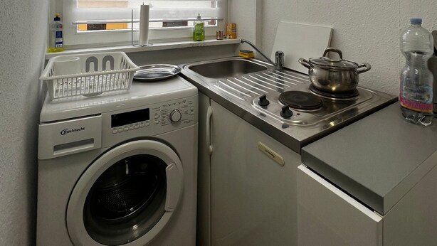 Una cucina compatta con lavatrice, lavello, fornello e un piccolo piano di lavoro.