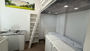 Una stanza compatta con angolo cottura, un letto, una scala a pioli e scaffalature.