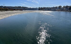 A beach with clear water reflecting sunlight, a sandy shore, and buildings in the background.
