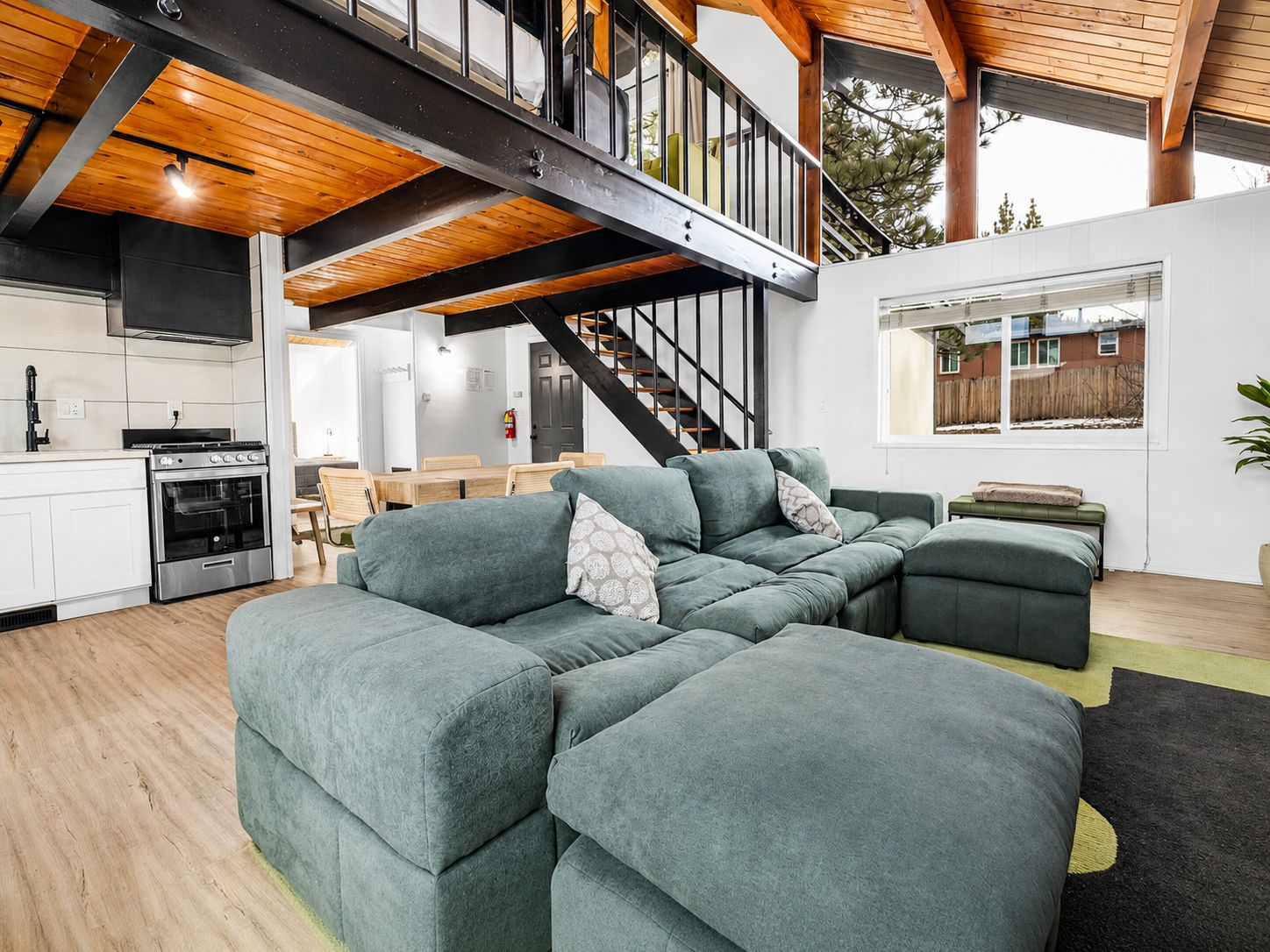 A modern interior with a sectional sofa, a staircase, and a kitchen area.