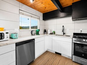 A modern kitchen with white cabinets, a wooden ceiling, a dishwasher, a stove, and a window with a view of the outdoors.