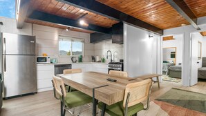 A modern kitchen with a wooden dining table, green upholstered chairs, and stainless steel appliances.