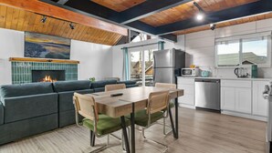 A modern kitchen with a wooden ceiling, a dining area with a table and chairs, a built-in stove, and a view of the outdoors through a window.