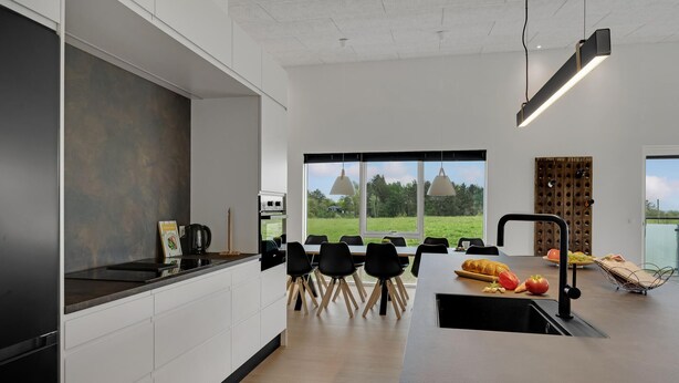 Eine moderne Küche mit einer großen Kochinsel, schwarzen Stühlen und Blick auf ein grünes Feld durch große Fenster.