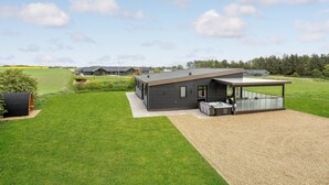 Ein modernes Haus mit überdachter Terrasse, Whirlpool und gepflegtem Rasen.