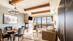 A spacious living room with a wooden dining table, comfortable seating, a fireplace, and a large window offering a scenic view. - Redstone Condo in Great Location, Hot Tub & Year-Round Recreation! Park City Newark 38 (Park City)