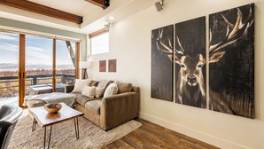 A spacious living room with a large window, a sofa, a coffee table, and a painting of deer on the wall. - Redstone Condo in Great Location, Hot Tub & Year-Round Recreation! Park City Newark 38 (Park City)