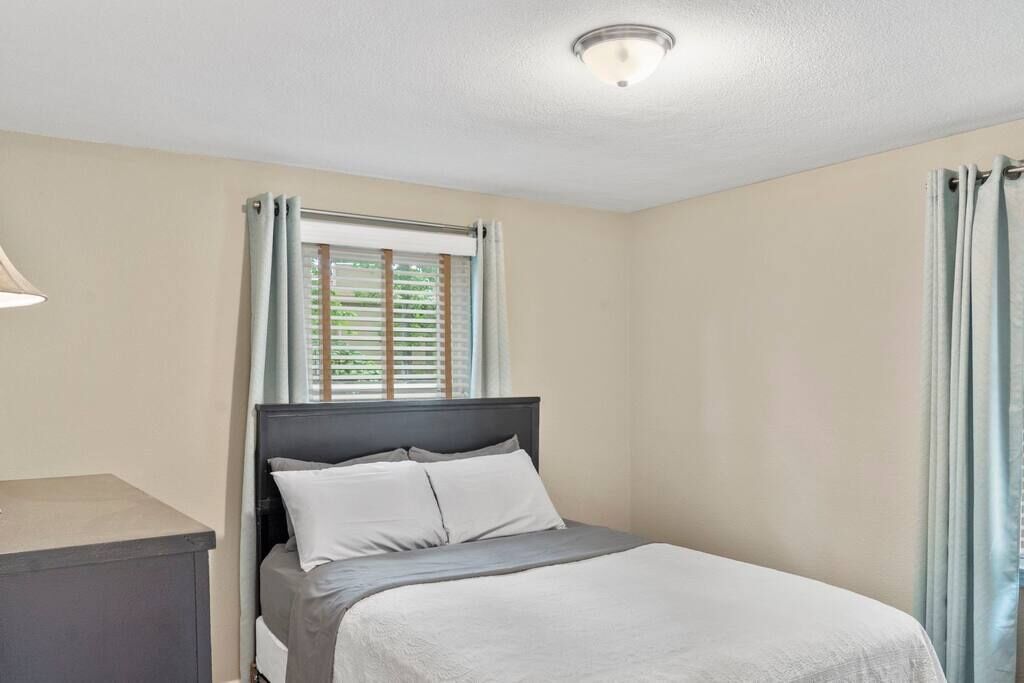 A bedroom with a bed, a nightstand, a window with curtains, and a ceiling light.