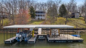 A dock with a covered area, a boat, and a house in the background.