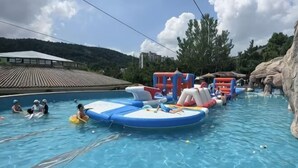 A swimming pool with inflatable water slides and a rocky landscape in the background. - China Magnetic Mountain Springs Park (Yantai)