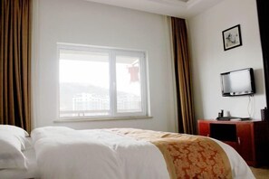 Una habitación de hotel con cama, televisión sobre un mueble y ventana con cortinas.