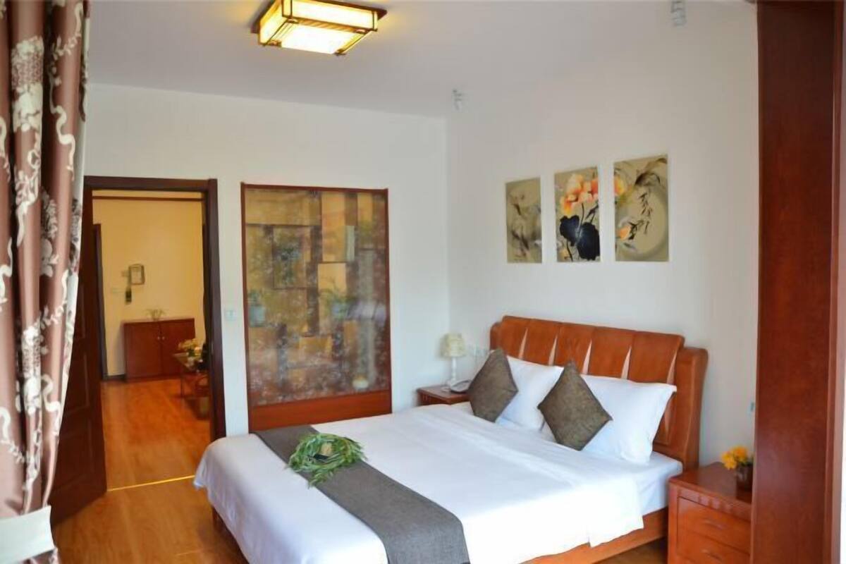 Een hotelkamer met een groot bed, een nachtkastje, een muur met kunstwerken en een deur die naar een andere kamer leidt.