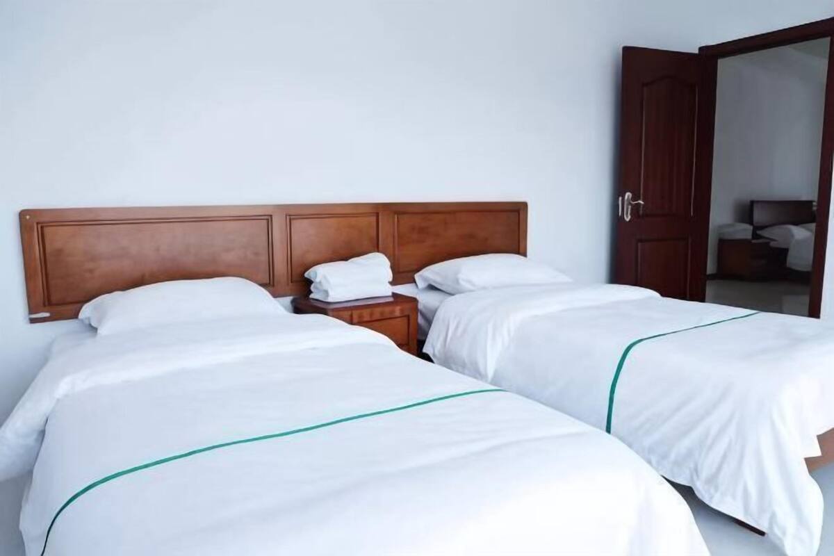 Een hotelkamer met twee bedden, een houten hoofdbord, een nachtkastje en een deur naar een andere kamer.