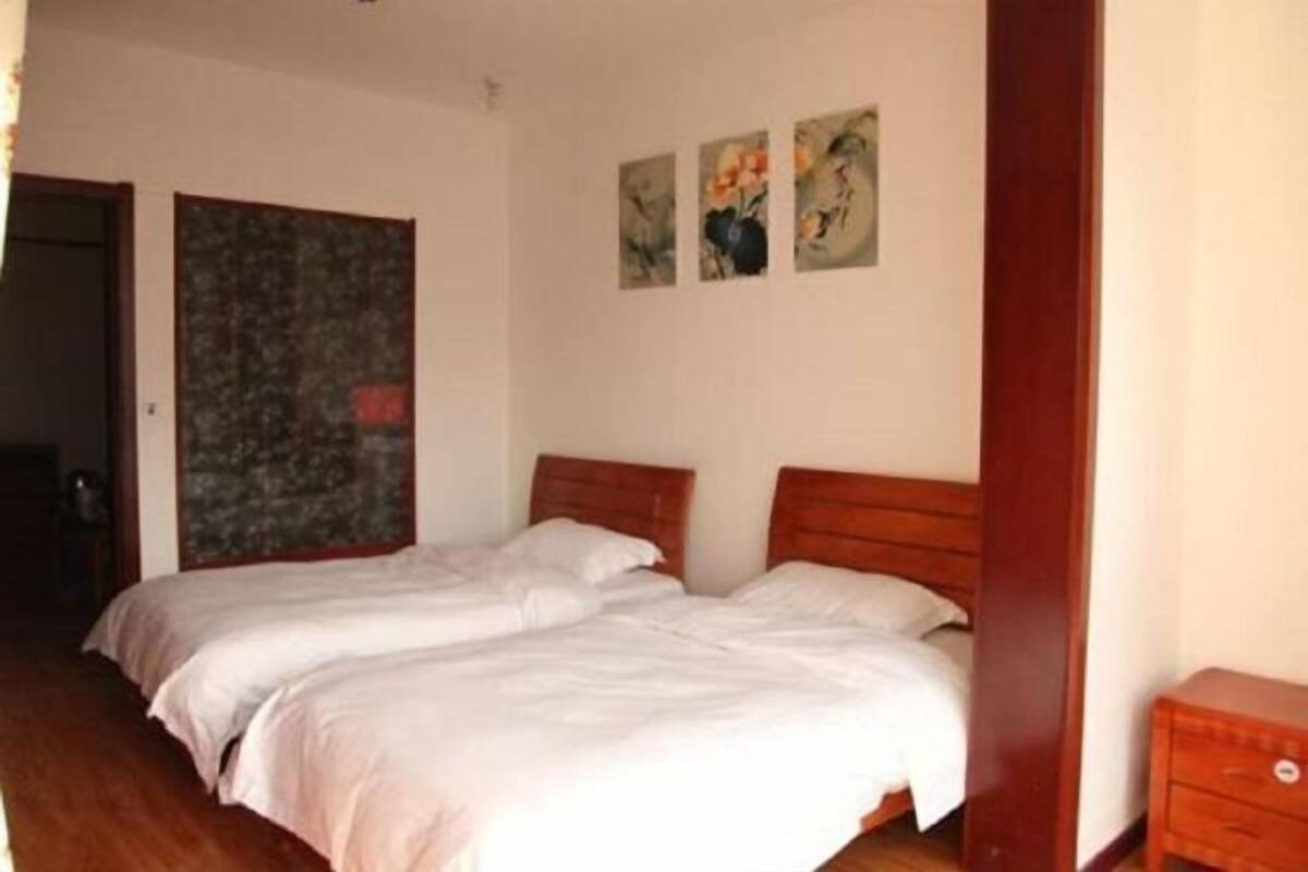 Een kamer met twee bedden, een houten hoofdbord, een klein nachtkastje en een deur.