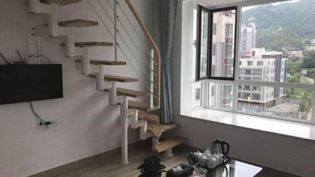 A modern apartment with a staircase, a flat-screen TV mounted on the wall, a dining table with chairs, and a large window offering a view of buildings and hills. - China Magnetic Mountain Springs Park (Yantai)