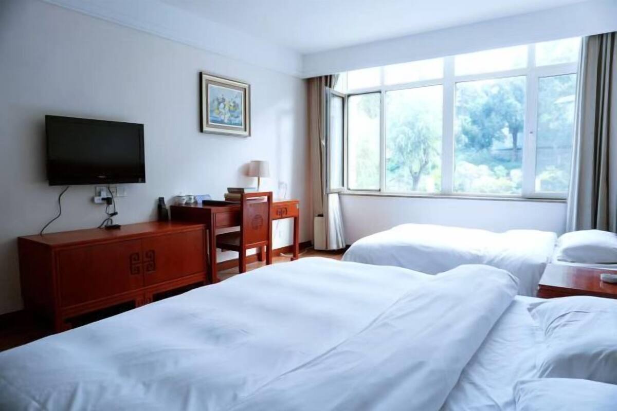 Een hotelkamer met twee bedden, een bureau, een televisie en een raam met uitzicht op bomen.