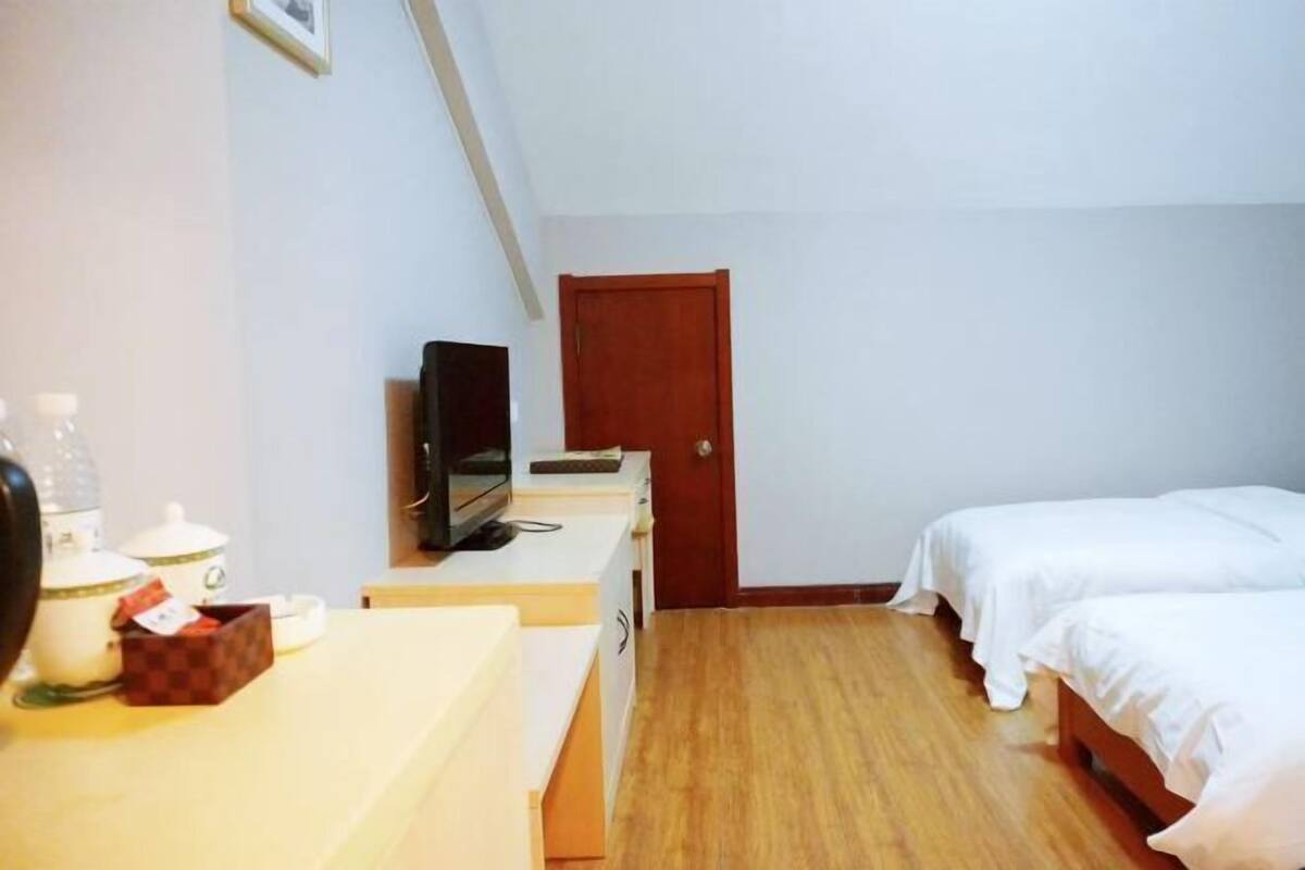 Een kamer met een bed, een bureau met een computer, een televisie en een deur.