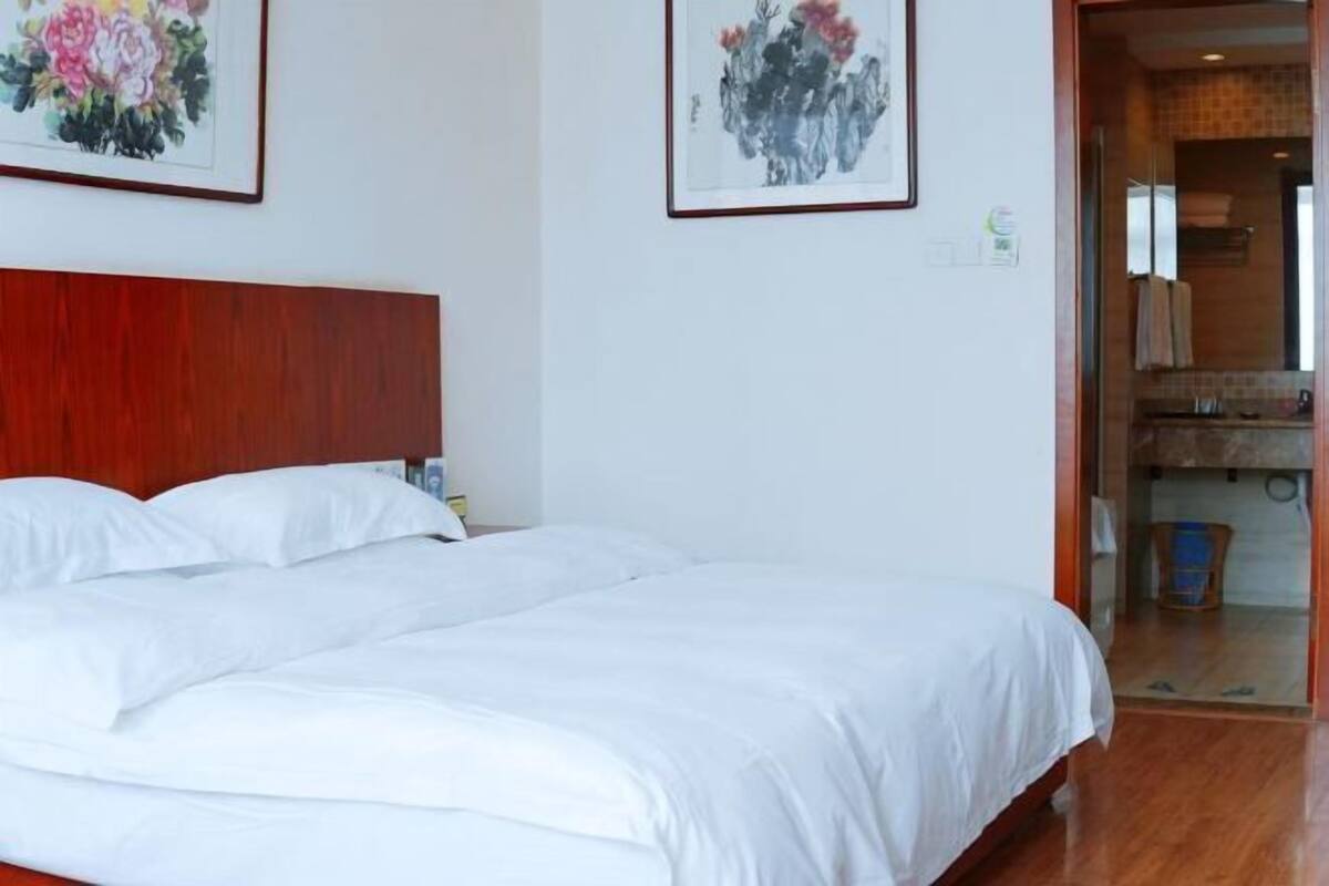 Een hotelkamer met een groot bed, een houten hoofdbord en twee ingelijste bloemstillevens aan de muur.