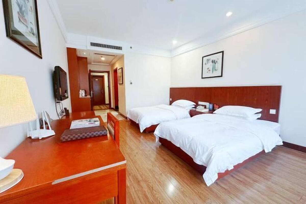 Een hotelkamer met twee eenpersoonsbedden, een houten bureau met lamp, een televisie en een lijst met een afbeelding aan de muur.