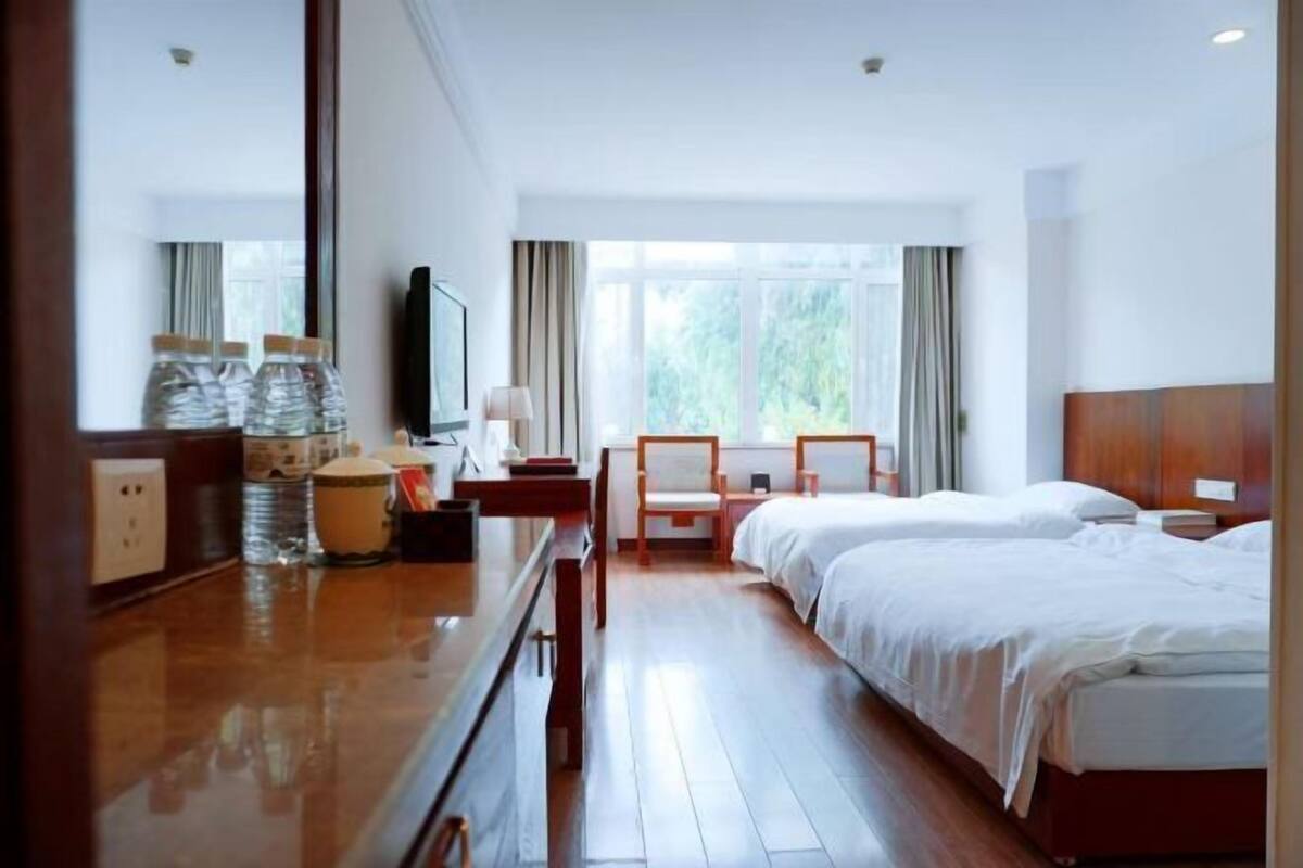 Een hotelkamer met een houten bureau, twee bedden, een televisie en een raam met gordijnen.